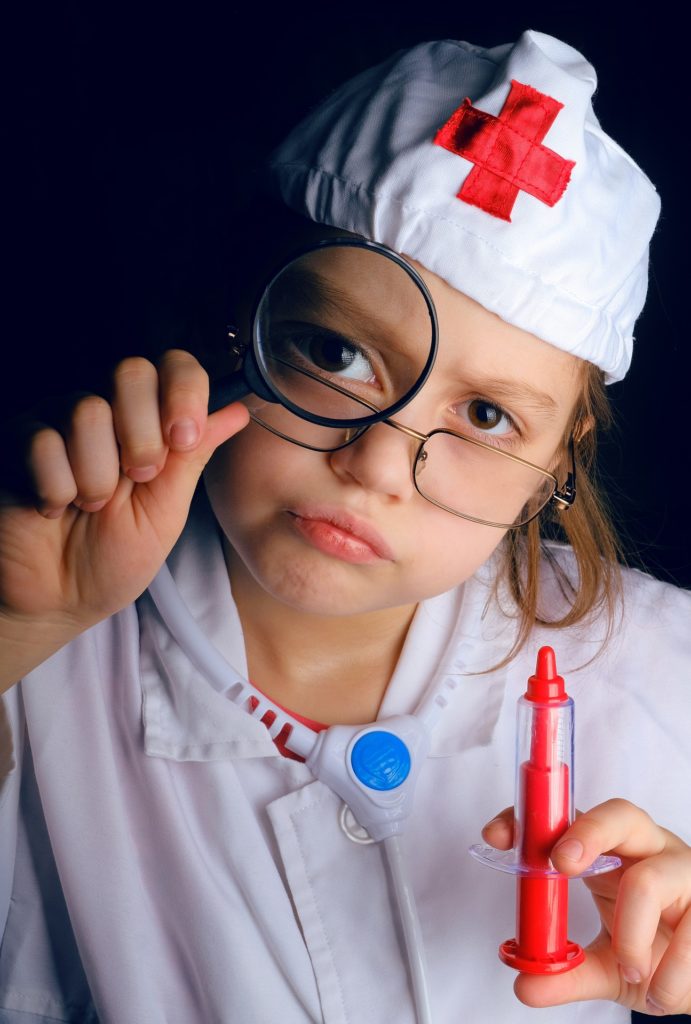 Petite fille déguisée en médecin qui tient une loupe devant ses yeux et une seringue en plastique dans l'autre main